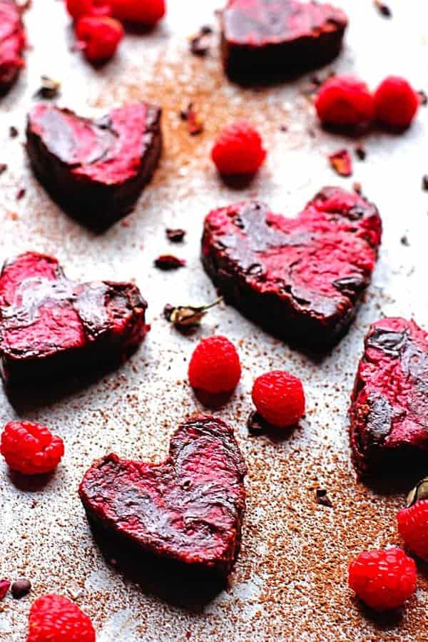 Heart shaped brownies scattered around with raspberries