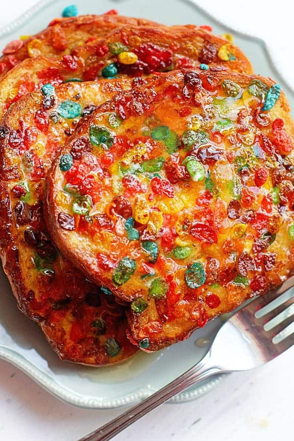 Close up of a stack of Fruity Pebbles French Toast served on a white plate with a fork