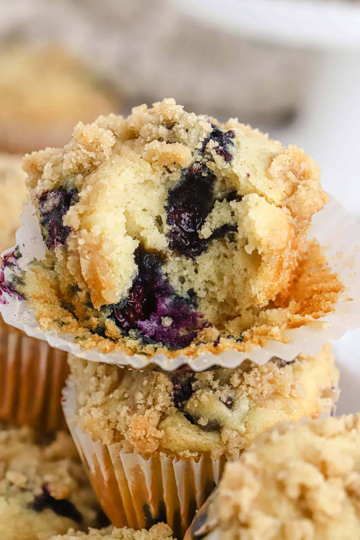 A blueberry streusel muffin on top of others with a bite taken to show the inside.