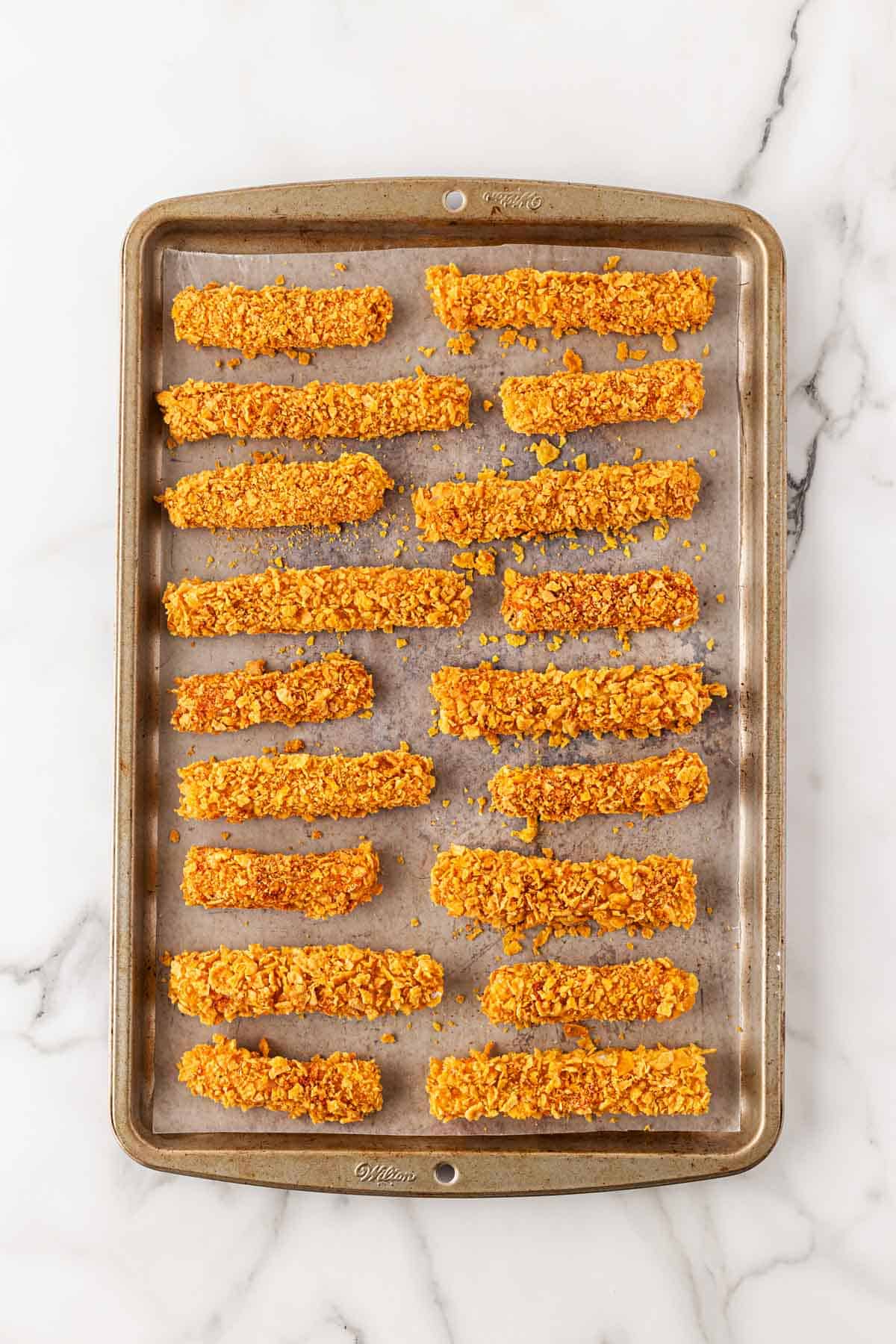 Fully coated fish strips placed on a parchment-lined baking sheet, ready for baking