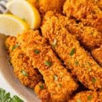 Baked fish sticks on a serving platter with parsley and lemon wedges