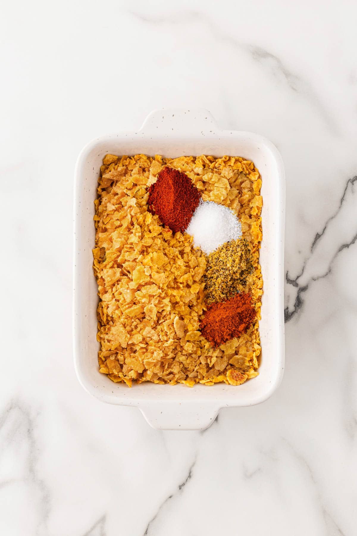 Small bowl filled with crushed cornflakes seasoned with paprika, salt, and pepper for coating the fish sticks