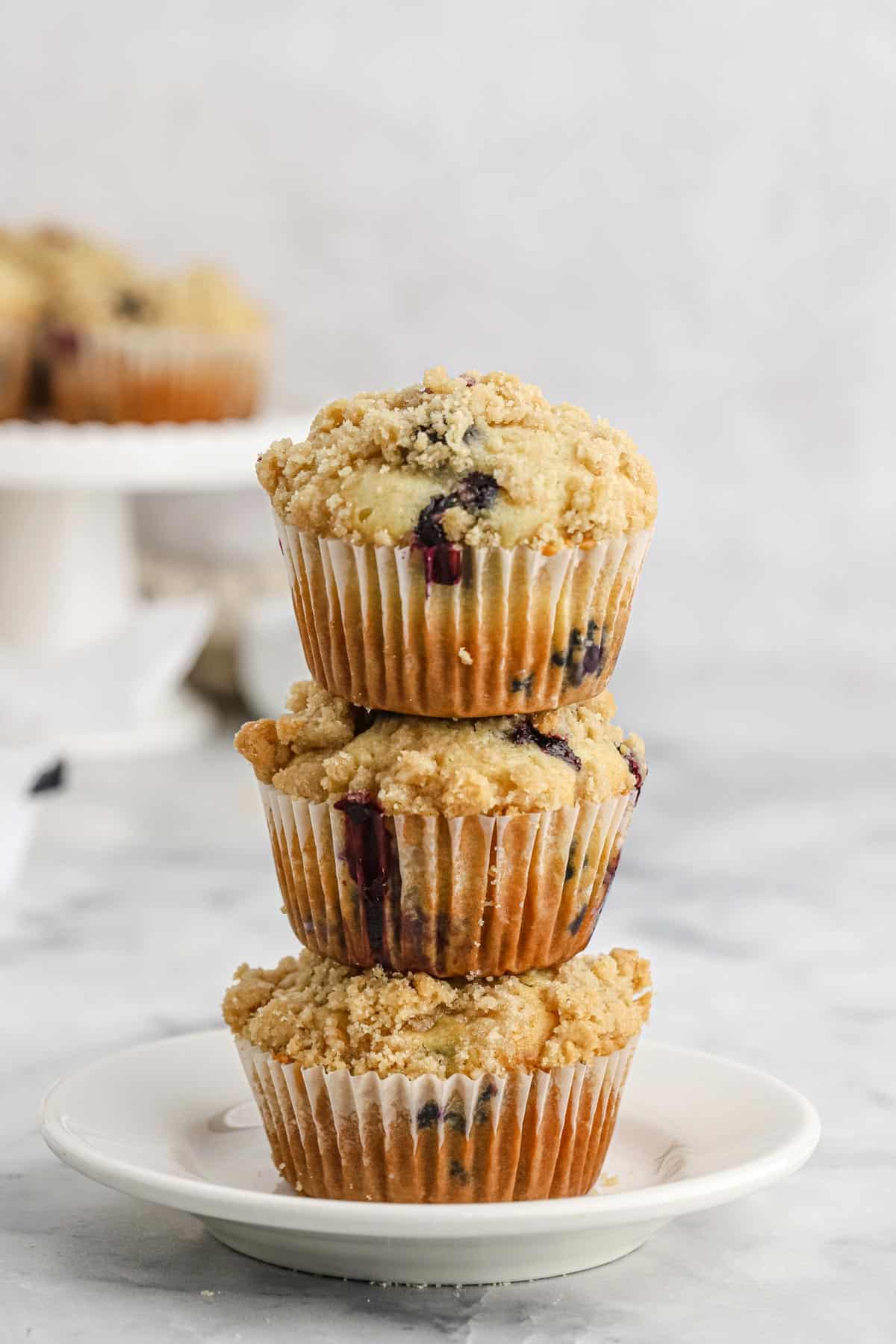 Three blueberry muffins with crumb topping stacked on top of each other.