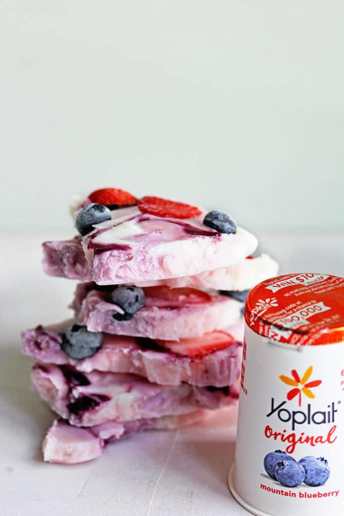 Close up of a stack of Frozen Yogurt Bark topped with strawberries, raspberries and blueberries and a container of yoplait yogurt