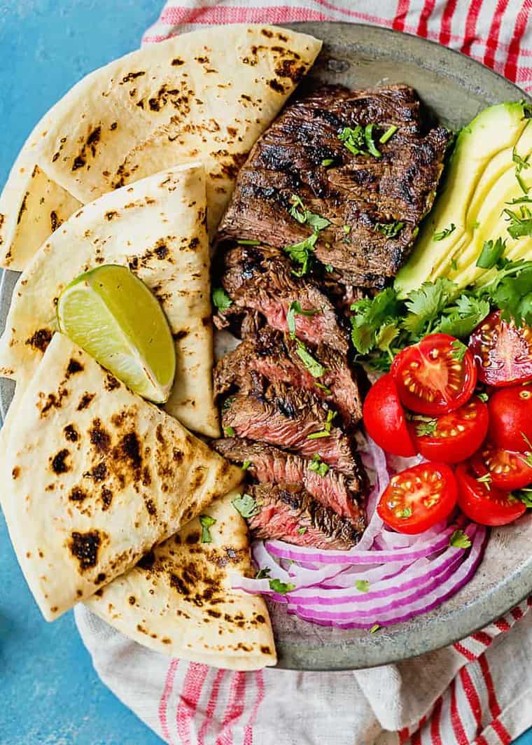 The best carne asada cut on a silver platter with tortillas, avocado, and veggies ready to serve
