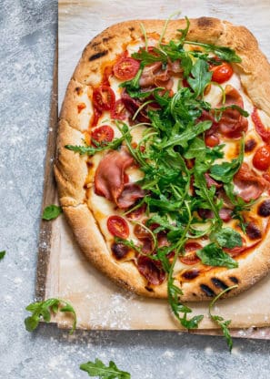 A whole Grilled Prosciutto Arugula Pizza served on a wooden cutting board