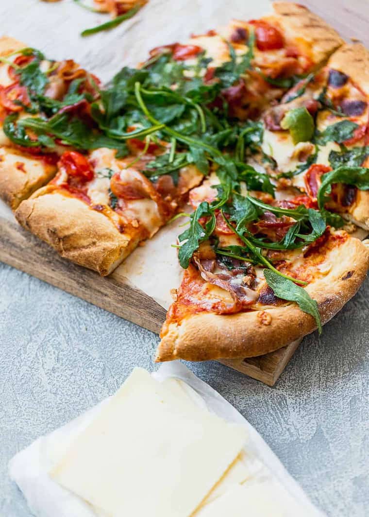 Grilled Prosciutto Pizza recipe cut into square slices with slices of cheese next to it