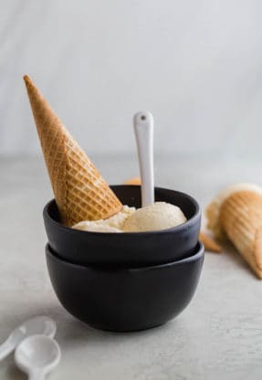 Two black bowls filled with homemade vanilla ice cream recipe with waffle cones ready to serve