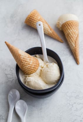 Delicious scoops of vanilla bean ice cream in black bowl with waffle cones with spoons ready to serve