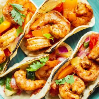 A close up of four shrimp tacos with salsa on a blue plate ready to serve