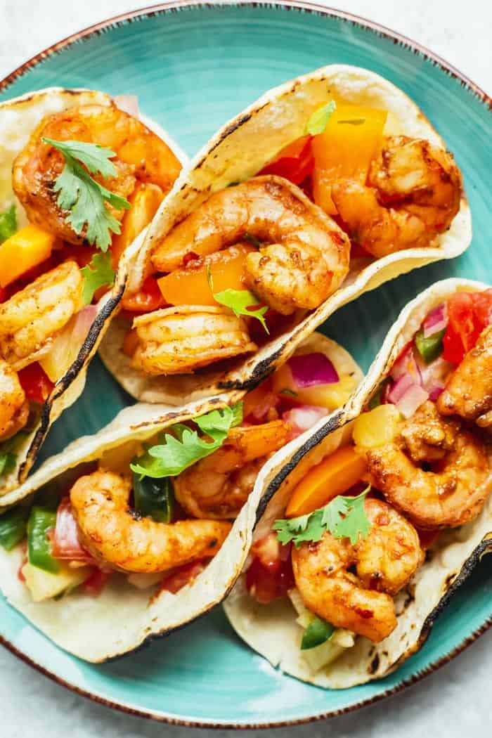 A close up of four shrimp tacos with salsa on a blue plate ready to serve