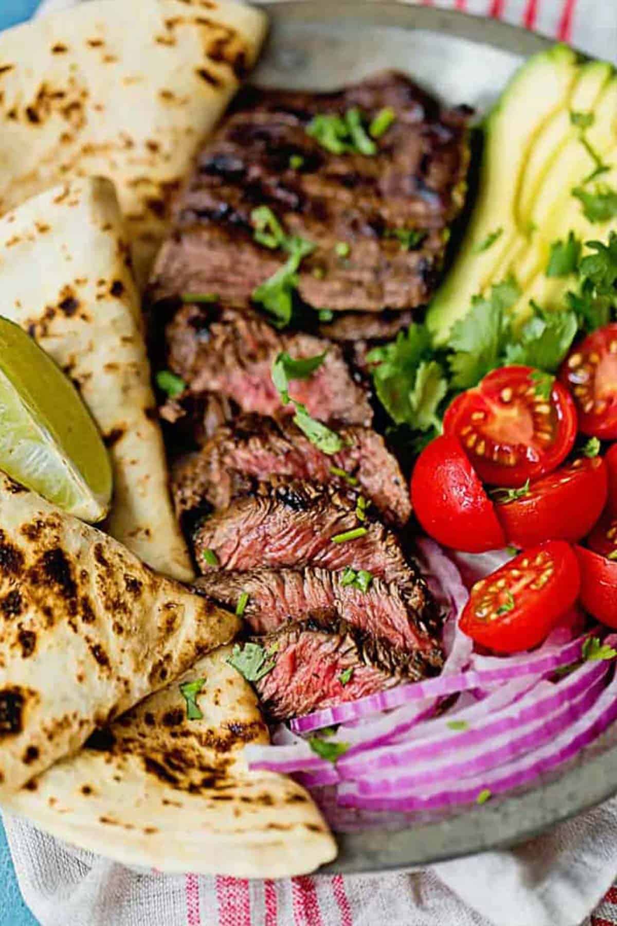 Marinated grilled skirt steak on platter with grilled tortillas, onions and tomatoes ready to serve for dinner.
