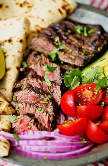 Grilled authentic carne asada steak sliced on a plate with tomatoes, avocado and flour tortillas close up