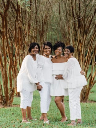 Jocelyn Delk Adams with her grandmother, mother and aunt all dressed in white under some trees
