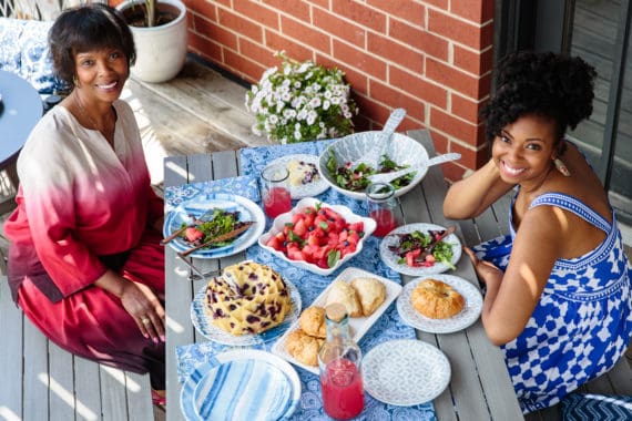 Jocelyn Delk Adams having her Weekly Brunch With Mom outdoors sitting at a picnic table with a Blueberry Orange Pound Cake, salad and other foods