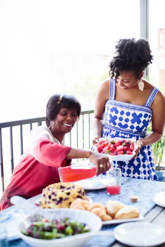 Jocelyn holding a fruit salad while her mom pours a beverage into a glass during their weekly brunch along with a Blueberry Orange Pound Cake