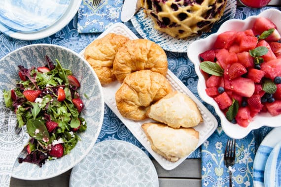 Overhead shot of salad, fruit salad, croissants and blueberry orange pound cake