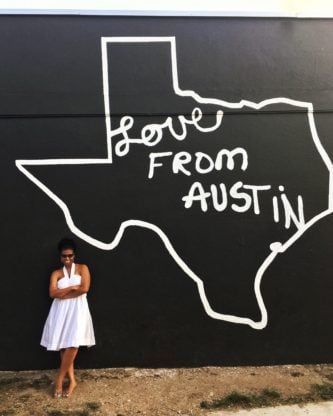 Jocelyn dressed in a sleeveless white dress standing next to a mural of the state of Texas with the words, "Love from Austin" on it