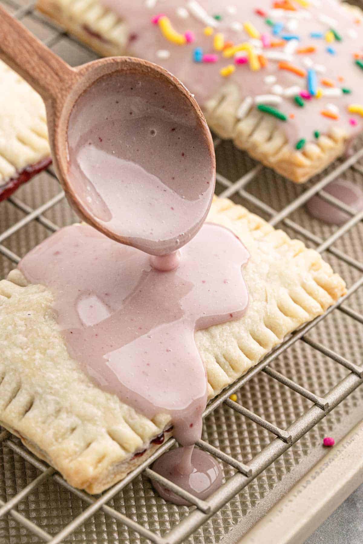 A spoon drizzling the glaze over the pop tarts.