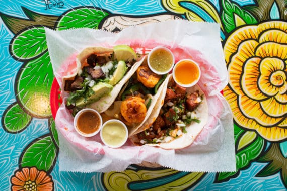 Shrimp tacos with four different salsas from Tacodeli on top of a beautiful flower painting in Austin