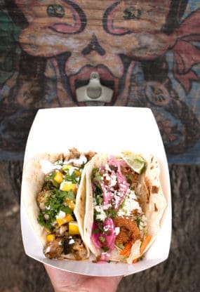 Two delicious tacos from Torchy's Tacos in Austin being held next to a mural 