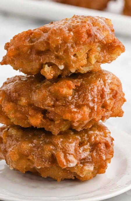 A stack of three apple fritters on a plate.