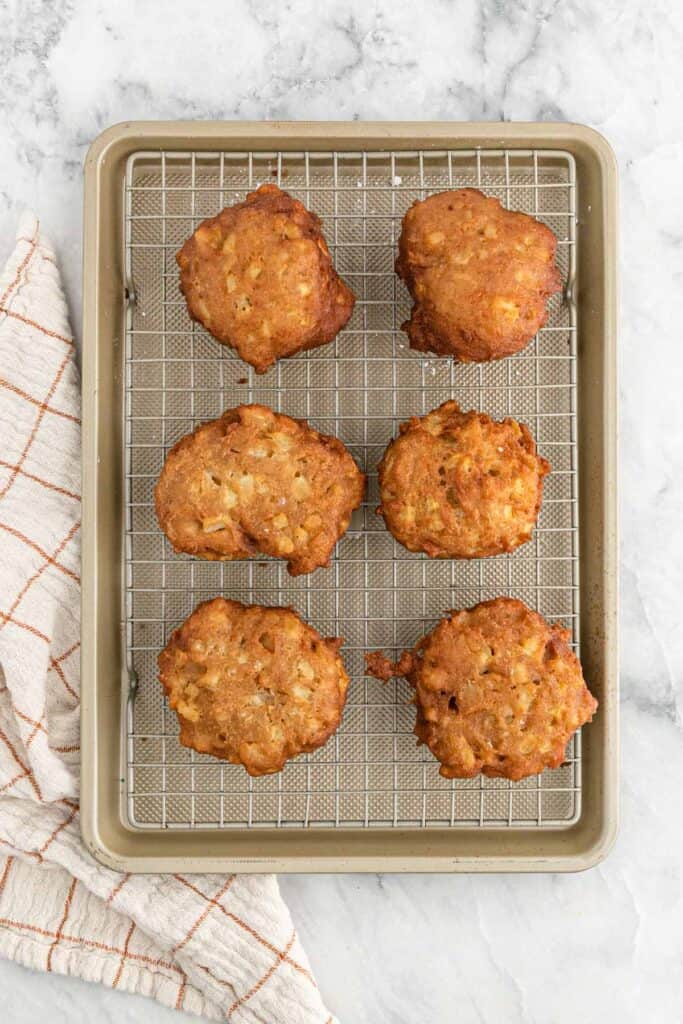 Cooked apple fritters draining on a wire rack on white countertop.