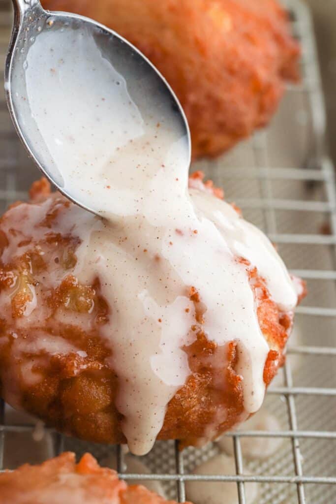 Drizzling the glaze over the top of an apple fritter