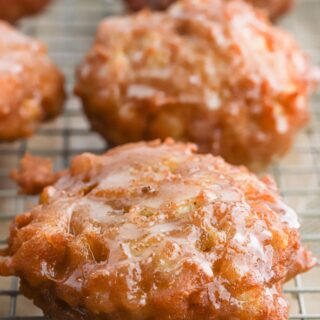 Glazed apple fritters on a wire rack.