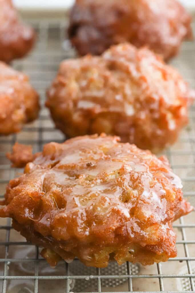 Glazed apple fritters on a wire rack.