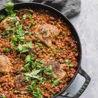 A cast iron skillet of spanish chicken and rice garnished with cilantro.