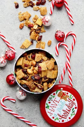 Chex mix recipe scattered across background with candy canes and ornaments for Christmas holiday