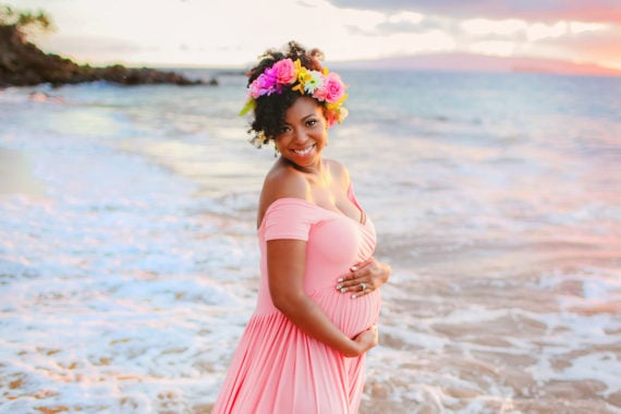 Jocelyn smiling on a beach in Maui dressed in a pink maternity dress at 30 weeks pregnant