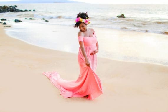 Jocelyn dressed in a pink maternity dress walking on a beach in Maui