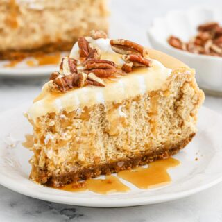 A slice of sweet potato cheesecake on a plate with caramel sauce and pecans on top.
