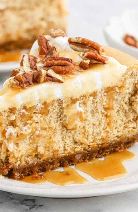 A slice of sweet potato cheesecake on a plate with caramel sauce and pecans on top.
