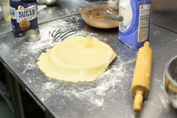 A pie crust and pie batter next to a rolling pin, sugar and flour