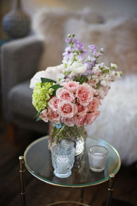 A beautiful boutique of flowers sitting on a glass table with glasses