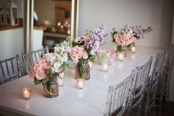 A white table with clear chairs and beautiful boutiques of flowers and lit candles