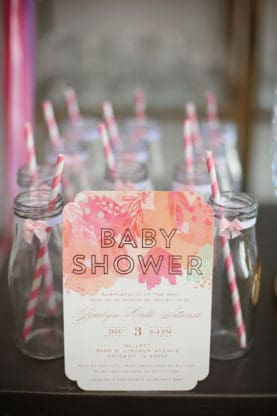 Several empty bottles with striped straws in them and a copy of the baby shower invite