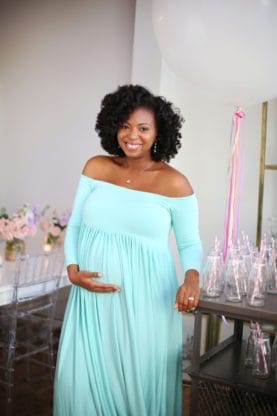 Jocelyn posing and holding her baby bump wearing a teal colored maternity dress