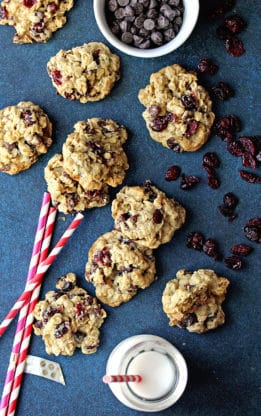 Overhead shot of several dark chocolate and cranberry oatmeal cookies with a bowl of chocolate chips and cranberries next to them