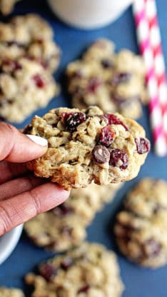 One dark chocolate and cranberry oatmeal cookie being held with more cookies in the background