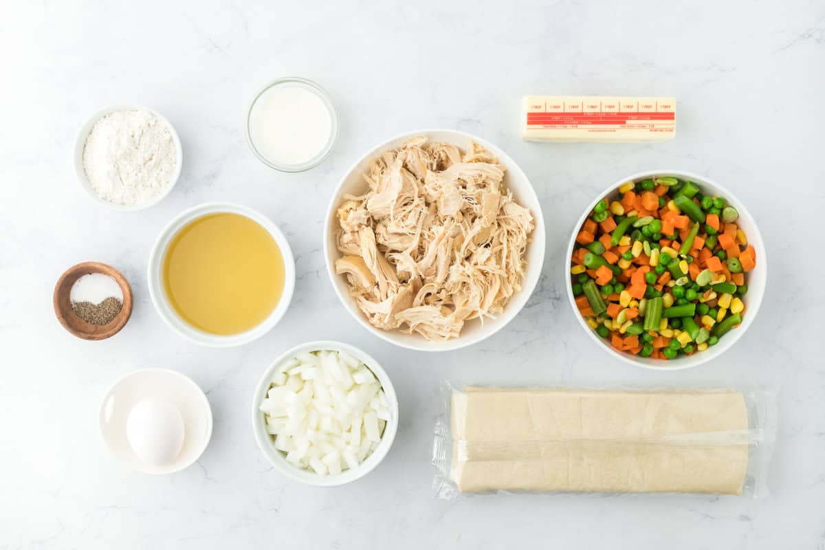 shredded chicken, mixed vegetables, butter, onion, chicken stock and seasonings in white bowls on a white background