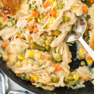 An overhead of the best chicken pot pie recipe with a spoon digging into the skillet on a white background with a striped napkin