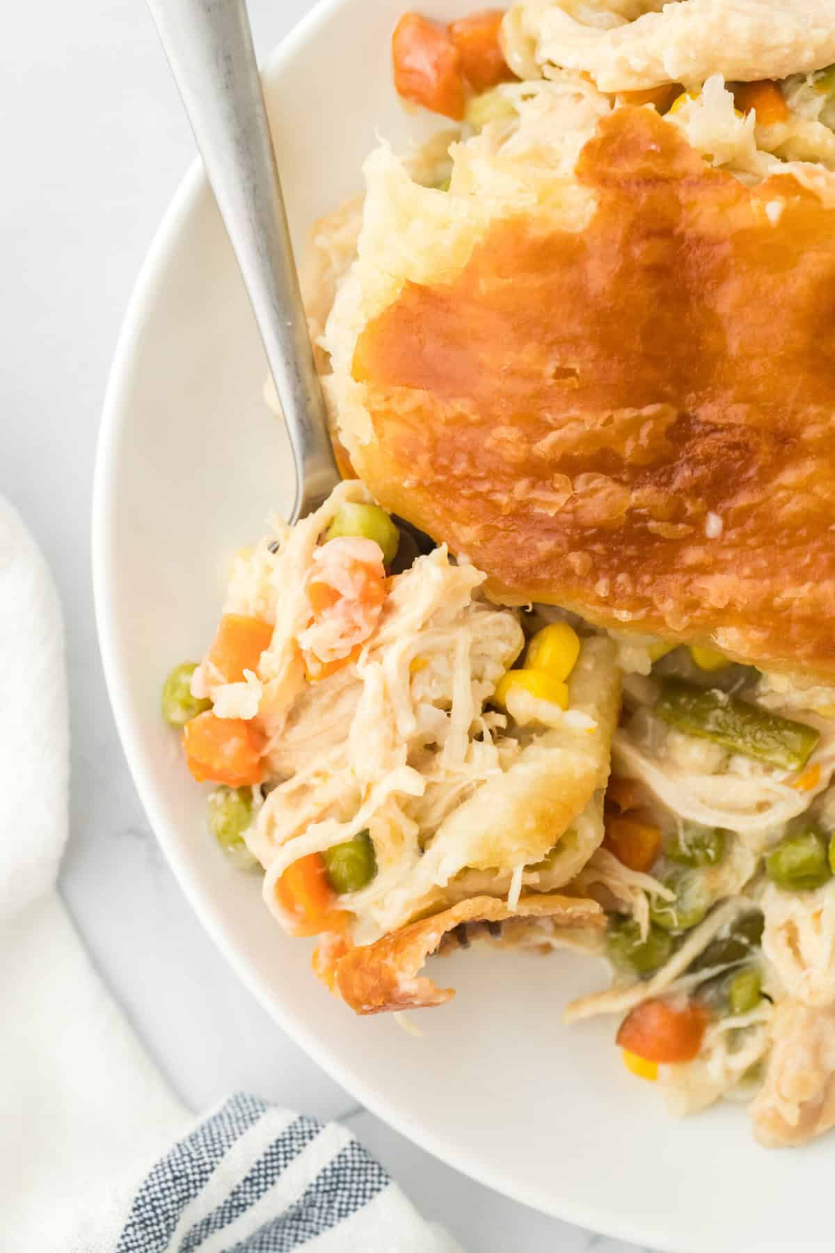 An overhead of puff pastry chicken pot pie on a white plate with a fork on white background