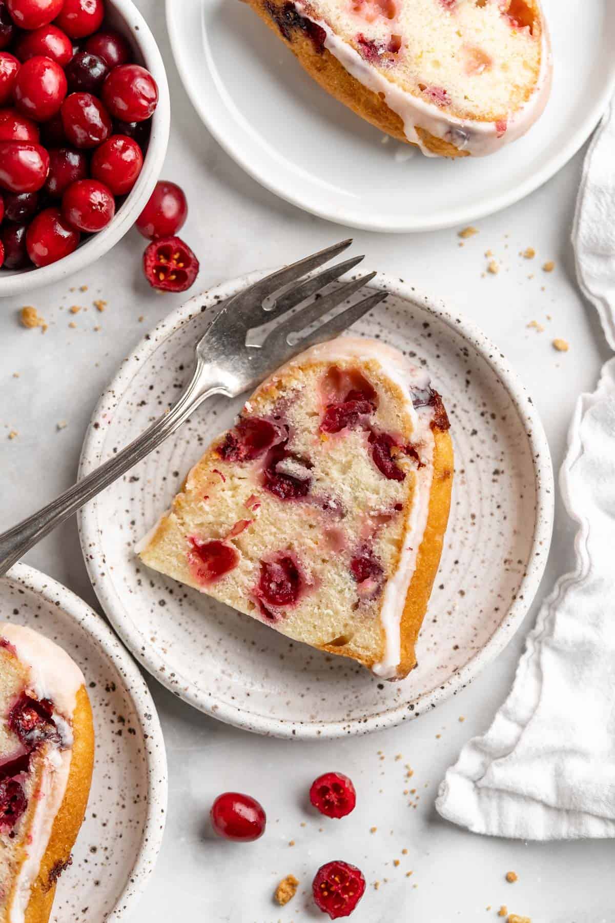 Plates of cranberry orange cake on the table with a bowl of berries on the table.