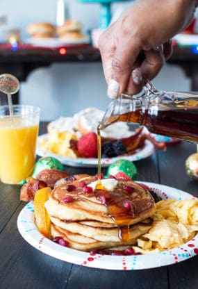 Orange Pancakes on plate with eggs and bacon with maple syrup being poured on top