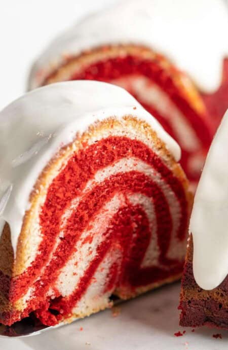 A spatula pulling out a slice of red velvet marble cake from the whole cake.