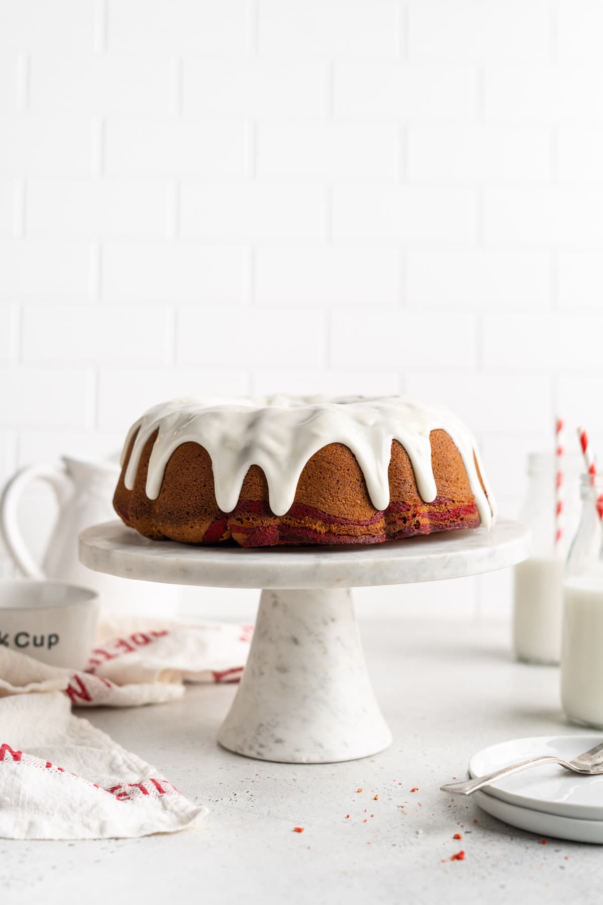 Red velvet marble pound cake on a white and gray marble stand with little jugs of milk in the background.